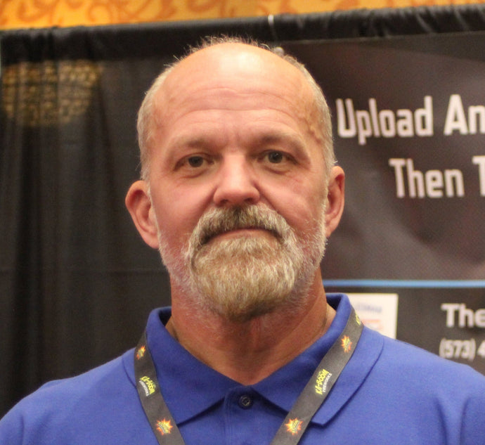 Man wearing a blue shirt with a lanyard, standing in front of a promotional backdrop.
